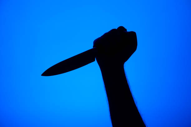 istock Knife stabbing gesture silhouette black on blue background studio shot unrecognizable 1302257404