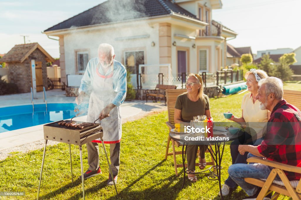 Elderly Neighbors Having Backyard Barbecue Party By The Swimming Pool