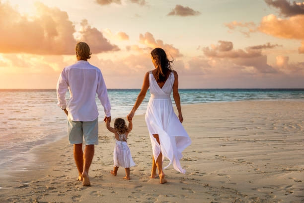 A family holding hands on vacation walks down a beac