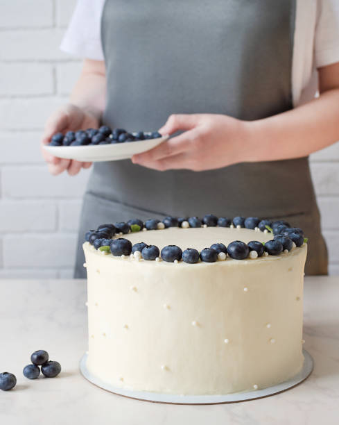 istock White cake with cream cheese and fresh blueberries. Confectioner decorating wedding cake with berries. 1302263742