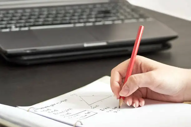 Photo of Young girl - female student writes homework from math at home. He writes in pencil in a notebook and counts formulas.