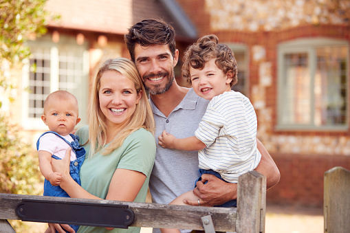Portrait Of Smiling Family Standing By Gate Outside Home In Countryside Together
