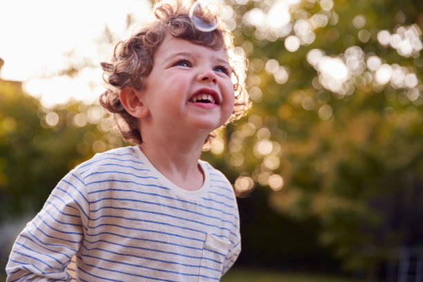 istock Young Boy Having Fun In Garden Chasing And Bursting Bubbles 1302265660