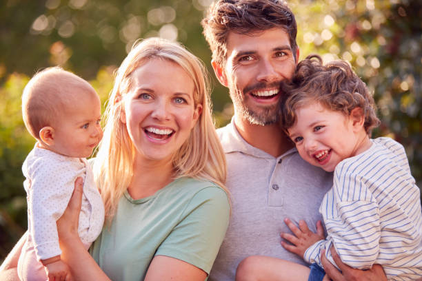 portrait of parents cuddling baby daughter and young son outdoors in garden in evening sun - babies and children close up horizontal looking at camera imagens e fotografias de stock