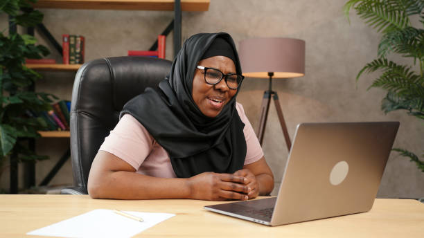 istock Plump lady in black hijab talks looking into laptop display 1302269130