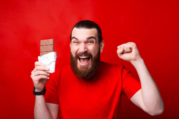 Handsome  amazed bearded man holding chocolate and gesturing, the best chocolate