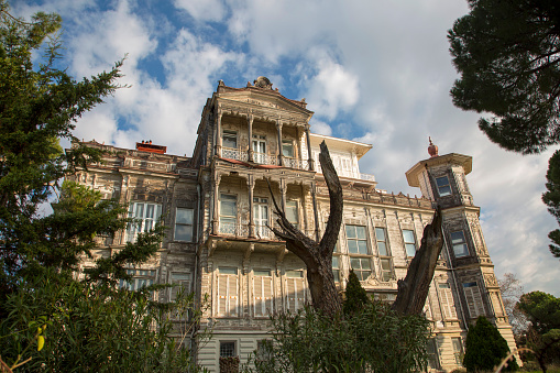 Istanbul, Turkey - December 31, 2020: View of the Ragip Pasha Mansion, one of the historical buildings of Istanbul, and its garden full of green trees. Cloudy blue sky on the background, horizontal close-up. Kadikoy Caddebostan coast. Ragip Pasha Mansion overlooks the Istanbul Princes' Islands.