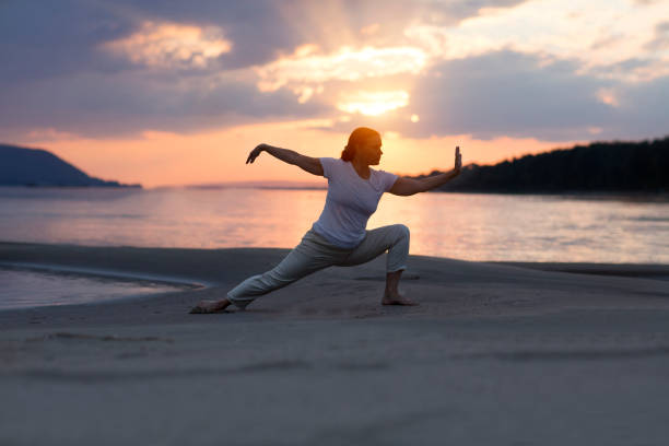 femme faisant le chuan de tai chi au coucher du soleil sur la plage.  activités de plein air en solo. distanciation sociale. concept de mode de vie sain. - tai chi photos et images de collection