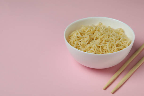 istock Bowl with noodles and chopsticks on pink background 1302283272