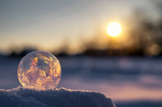 Iced soap bubble on snow with sun in the background
