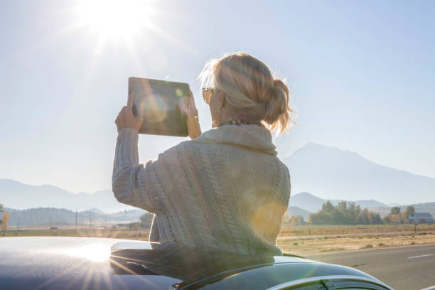 Woman takes photo with digital tablet from car sunroof Sun illuminates mountains and car mt shasta photos stock pictures, royalty-free photos & images