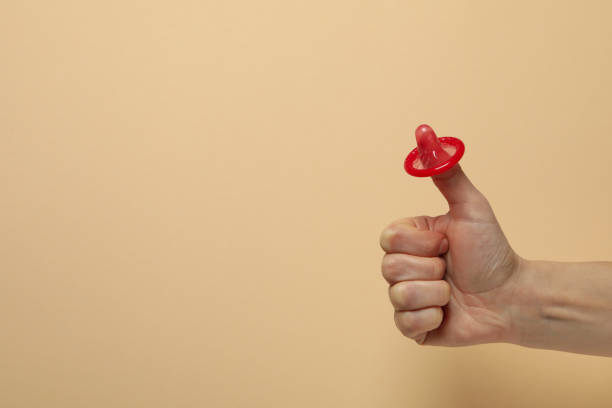 istock Female arm with red condom on beige background, space for text 1302285975