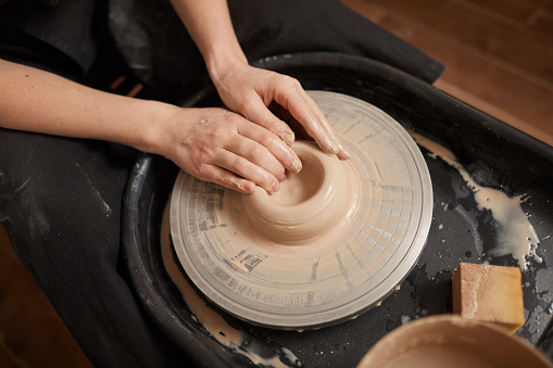 High angle close up of elegant female hands shaping clay on pottery wheel in workshop, copy space