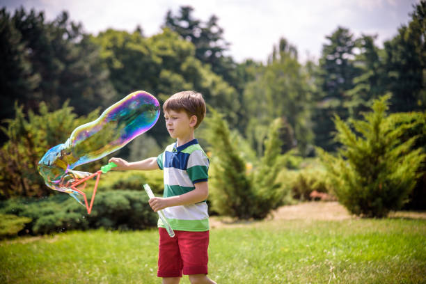 niño jugando con sus burbujas de jabón juguete en el parque. actividad infantil. concepto primaveral - child dancing preschooler outdoors fotografías e imágenes de stock