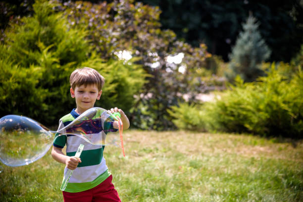 niño jugando con sus burbujas de jabón juguete en el parque. actividad infantil. concepto primaveral - child dancing preschooler outdoors fotografías e imágenes de stock