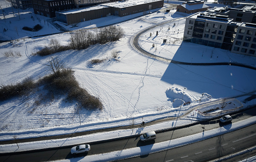 Aerial view of road with cars driving. Winter with snow covered landscape. Foot steps across parking lot