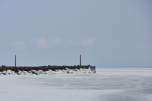 Lonely stony shore with beacons surrounded by snowy ice water under cloudy blue sky in cold day