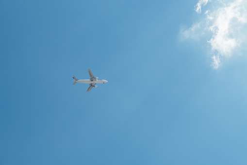 Plane flying through the empty blue sky illuminated by the sun with clouds in the background