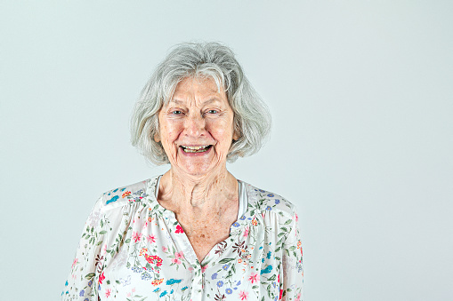 Elderly woman in her 80's with Gray hair isolated on a white backdrop smiling and laughing and happy from the shoulders up.