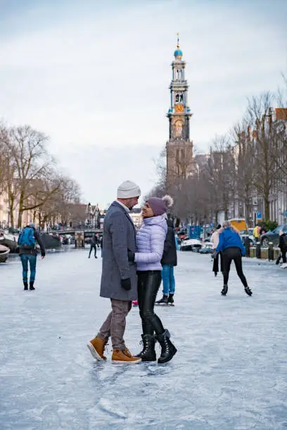 couple visit Amsterdam during Winter with people Ice skating on the canals in Amsterdam the Netherlands in winter, frozen canals in Amsterdam during winter.