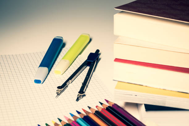 istock A stack of books in the foreground, a drawing compass rests on the desk, highlighters and colored crayons are placed on a sheet of squares. 1302297916