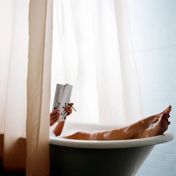 Woman in bubble bath relaxing reading doing crossword puzzle.. Woman in bubble bath relaxing reading doing crossword puzzle. free standing bath stock pictures, royalty-free photos & images
