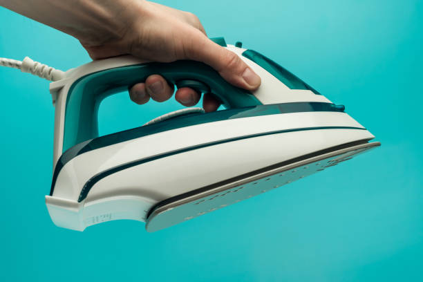 istock a man's hand holds an iron on a blue background. a man performs women's work at home. a man irons clothes 1302300707