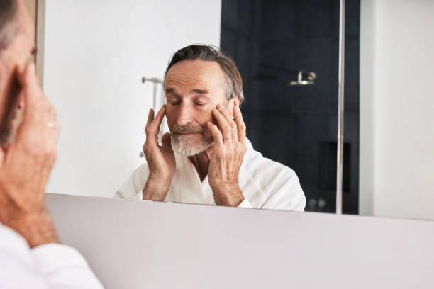istock Senior man massaging his face while standing in front of a mirror in bathroom 1302302159