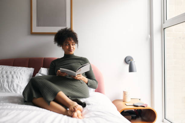 istock Young Woman Lying And Relaxing On Bed At Home Reading Book 1302302372