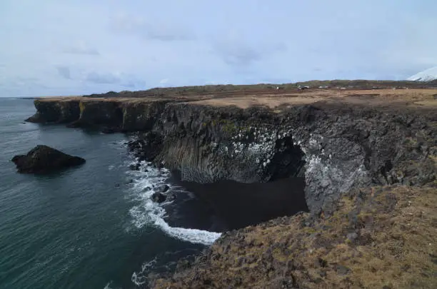 Tide going out on a black sand beach with basalt columns.