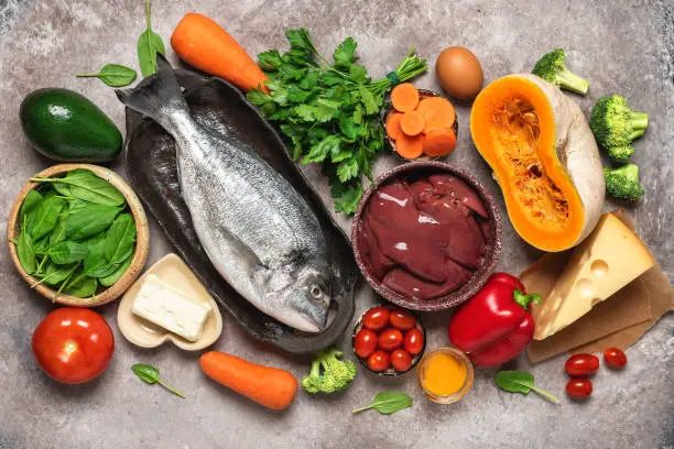 Photo of Healthy balanced food background. Foods rich in vitamin A. Turkey liver, vegetables, fresh fish, butter and cheese. Top view, flat lay.