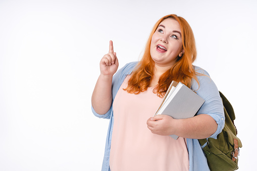 Fat ginger-haired woman having an idea with backpack isolated over white background