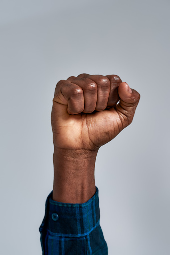 Close up shot of raised fist of african american guy in checkered shirt posing isolated over gray background. Social issues concept