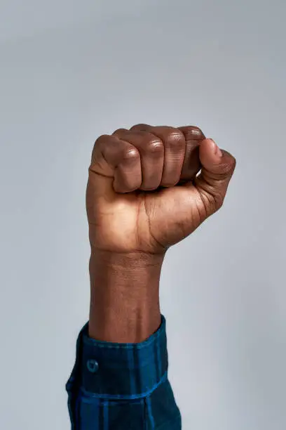 Photo of Close up shot of raised fist of african american guy in checkered shirt posing isolated over gray background