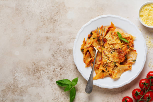 istock Pasta Maltagliati with classic tomato sauce, parmesan and basil on a rustic concrete light table background. Traditional Italian dish serving. Top view. 1302312192