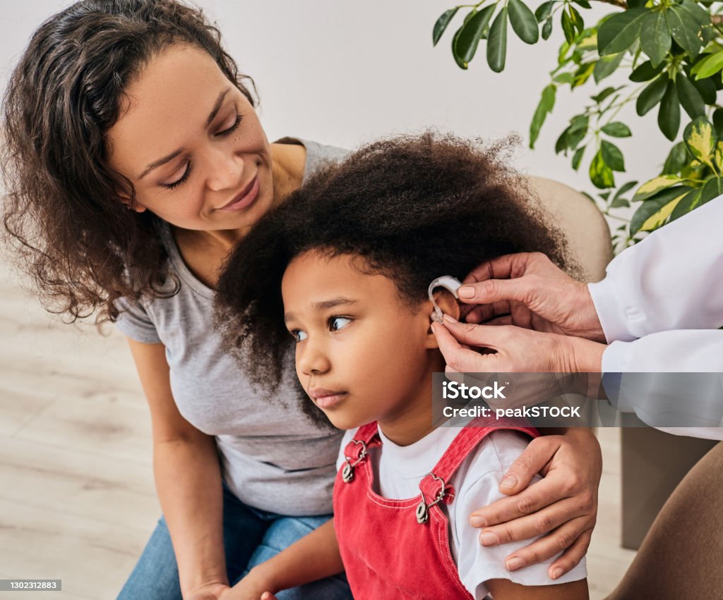 Cute girl with her mother during install hearing aid by her audiologist. Hearing treatment for a child Hearing Aid Stock Photo