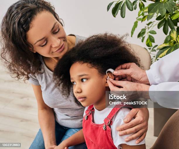 Cute Girl With Her Mother During Install Hearing Aid By Her Audiologist Hearing Treatment For A Child Stock Photo - Download Image Now
