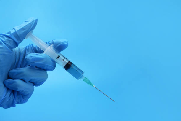 istock Hand holding syringe with medicine on a blue background 1302315596