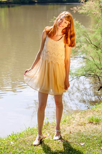 Front view of happy young attractive woman with long red hairs. Blurred background of the pond and green nature. She is very happy, singing and dancing. Summer atmosphere.
