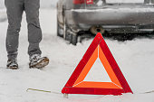 Warning road sign Triangle close-up on the background of a man's legs, car. Winter travel, road problems, concept. Selective Focus