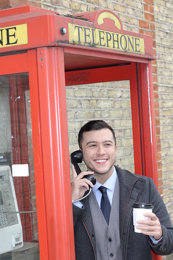 Ethnic businessman calling in classic red phone booth.