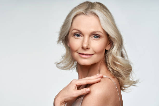 mulher mais velha e madura atraente olhando para a câmera isolada em fundo branco anunciando tratamento de spa skincare. mid age tightening face care rejuvenats conceito de cosméticos. retrato - fashion model blond hair women beauty - fotografias e filmes do acervo