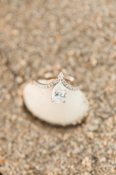 istock Macro Photo Teardrop Diamond Engagement Ring on a Seashell on the Sandy Beach 1302326204