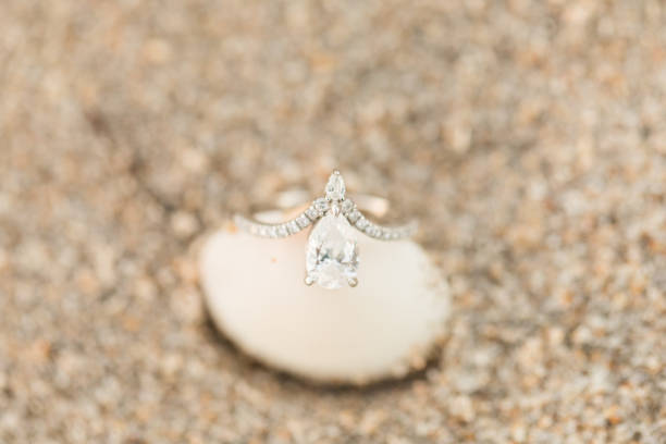 istock Macro Photo Teardrop Diamond Engagement Ring on a Seashell on the Sandy Beach 1302327039