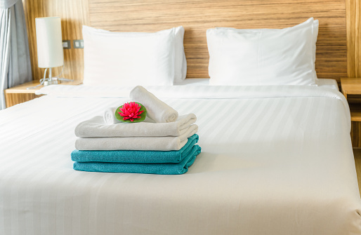 Stack of fresh white and blue towels with red lotus flower on white bed in bedroom.