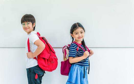 Back to school for concept. Boy and girl school children with backpack standing in white classroom on whiteboard background.