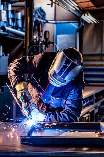 Worker in protective mask welding pipe in workshop