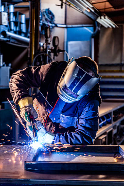 A welder welding in factory The welder performs welding task at his workplace in the factory, while the sparks "fly" around, he wears a protective helmet. welding photos stock pictures, royalty-free photos & images
