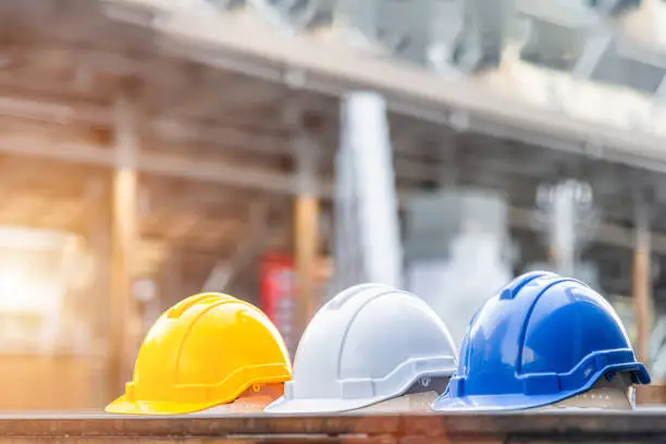 Photo of Yellow, white and blue hard safety helmet hat for safety project of worker, foreman or engineer and electrician on the concrete floor
