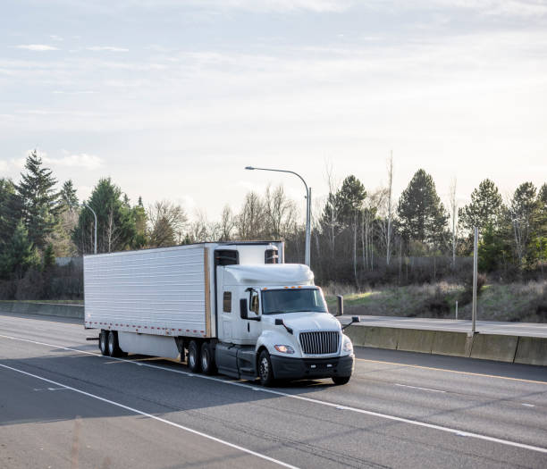 istock Big rig low cab white semi truck transporting cargo in refrigerated semi trailer running for delivery on the wide divided highway road 1302331262